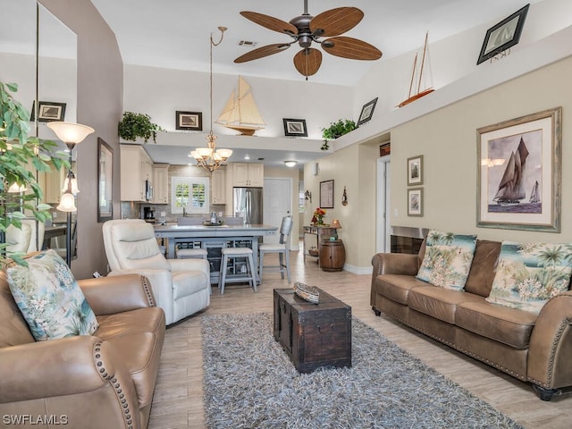 living room featuring high vaulted ceiling, ceiling fan with notable chandelier, and light hardwood / wood-style flooring