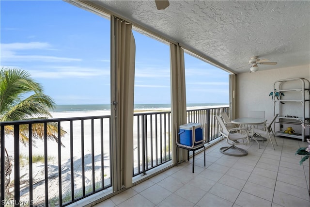 sunroom featuring a beach view, ceiling fan, and a water view