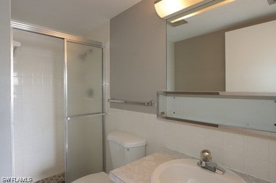 bathroom with toilet, a shower with door, tasteful backsplash, and sink