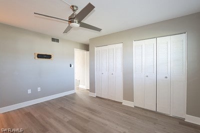 unfurnished bedroom with hardwood / wood-style floors, ceiling fan, and multiple closets