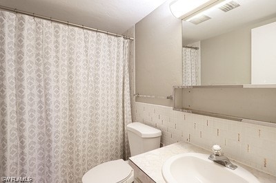 bathroom with vanity, backsplash, toilet, and tile walls