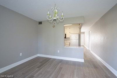 unfurnished room with hardwood / wood-style flooring and an inviting chandelier