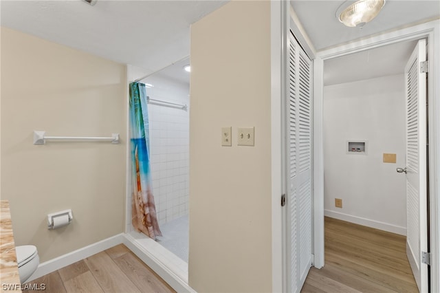 bathroom featuring a shower stall, baseboards, wood finished floors, and toilet