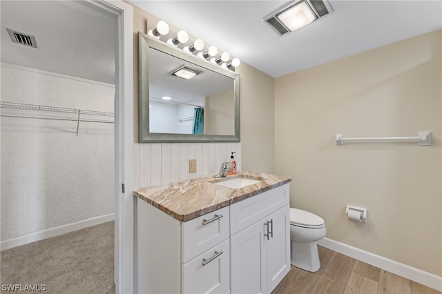 bathroom with visible vents, a walk in closet, toilet, vanity, and wood finished floors