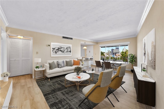 living area featuring crown molding, visible vents, light wood finished floors, and a textured ceiling