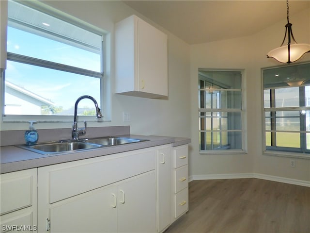 kitchen with sink, wood-type flooring, hanging light fixtures, and white cabinetry