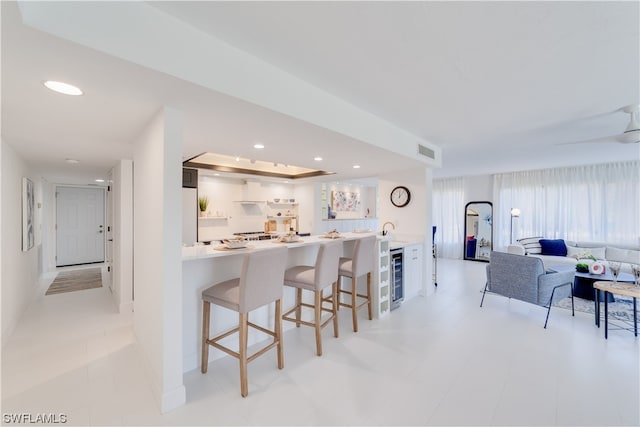 kitchen featuring beverage cooler, a kitchen breakfast bar, sink, kitchen peninsula, and white cabinetry