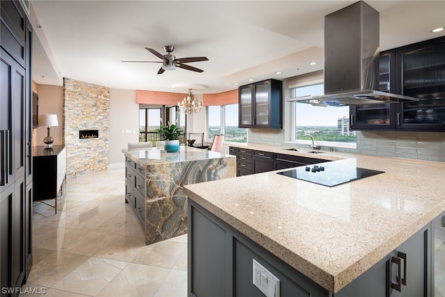 kitchen featuring tasteful backsplash, range hood, a kitchen island, and ceiling fan with notable chandelier