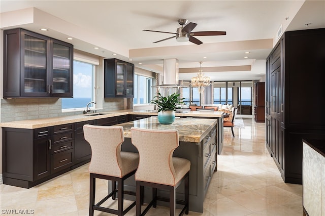 kitchen featuring light tile floors, a kitchen island, light stone countertops, ceiling fan with notable chandelier, and backsplash