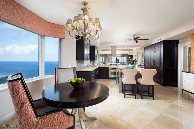 dining room with light tile floors, a raised ceiling, ceiling fan with notable chandelier, and a water view