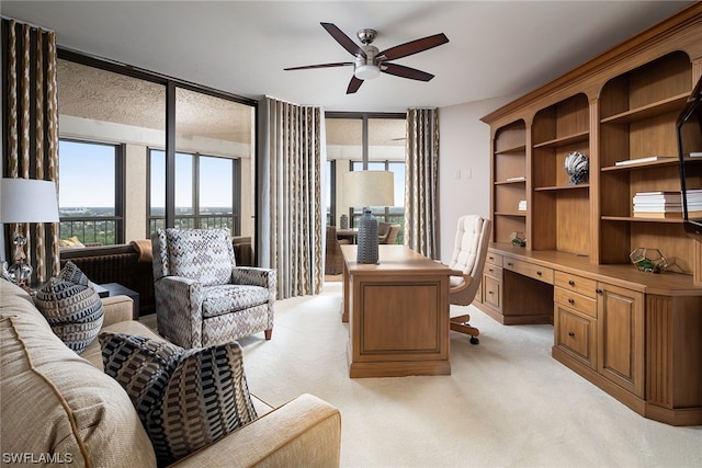 office area with expansive windows, light colored carpet, ceiling fan, and built in desk