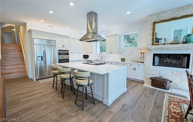 kitchen featuring light stone counters, appliances with stainless steel finishes, island range hood, white cabinetry, and a center island