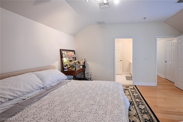 bedroom featuring connected bathroom, vaulted ceiling, and light wood-type flooring