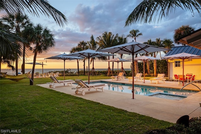 pool at dusk with a patio area and a lawn