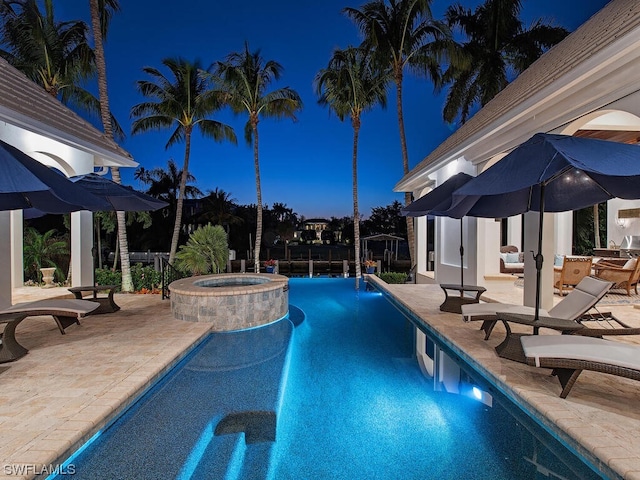 pool at night with an in ground hot tub and a patio