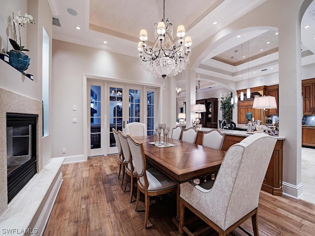 dining area featuring a raised ceiling, a high ceiling, a chandelier, and light wood-type flooring