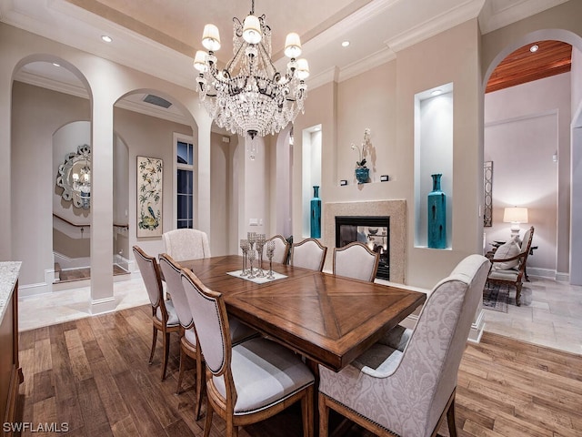 dining space with a multi sided fireplace, an inviting chandelier, crown molding, and light hardwood / wood-style flooring