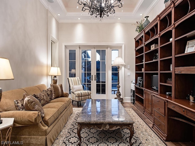 living room with a notable chandelier, french doors, ornamental molding, a tray ceiling, and light wood-type flooring