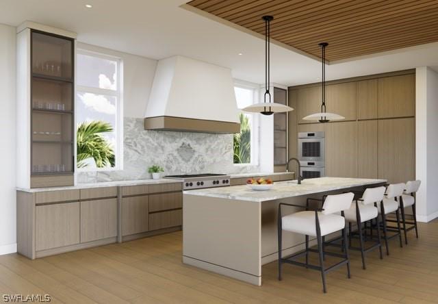 kitchen with a breakfast bar area, double oven, backsplash, decorative light fixtures, and custom exhaust hood