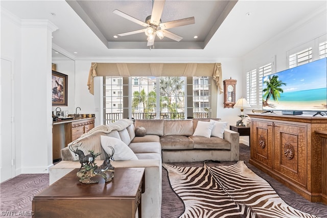 living room featuring ceiling fan, ornamental molding, a tray ceiling, and carpet