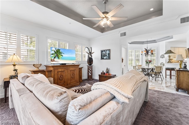 living room featuring ceiling fan with notable chandelier and a tray ceiling