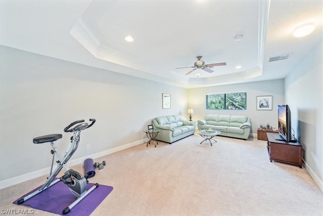 exercise room with ornamental molding, light colored carpet, ceiling fan, and a tray ceiling