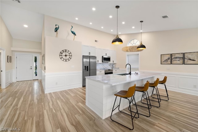 kitchen with light hardwood / wood-style flooring, appliances with stainless steel finishes, white cabinets, hanging light fixtures, and light stone counters