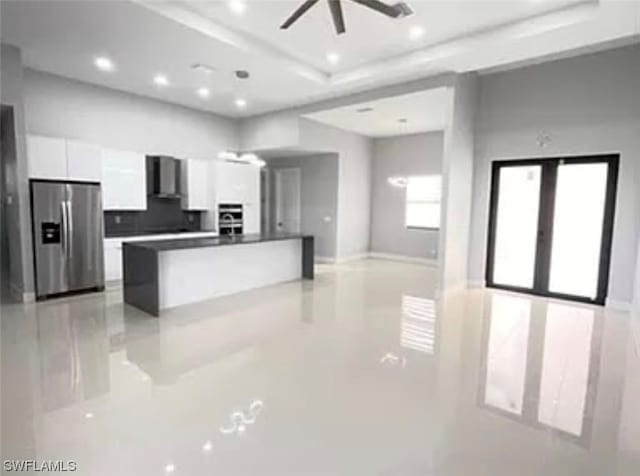 kitchen featuring wall chimney range hood, ceiling fan, stainless steel refrigerator with ice dispenser, and white cabinetry