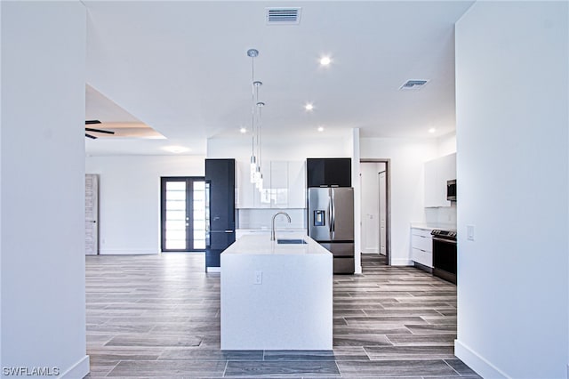 kitchen featuring an island with sink, ceiling fan, appliances with stainless steel finishes, dark wood-type flooring, and decorative light fixtures