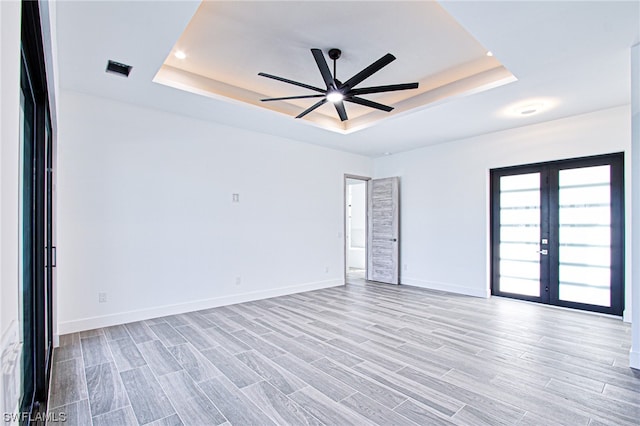 empty room featuring french doors, ceiling fan, a raised ceiling, and light hardwood / wood-style flooring