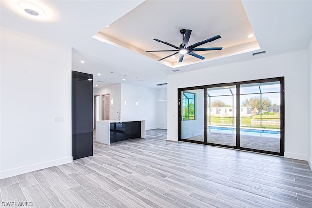 unfurnished living room featuring a raised ceiling, sink, ceiling fan, and light hardwood / wood-style flooring