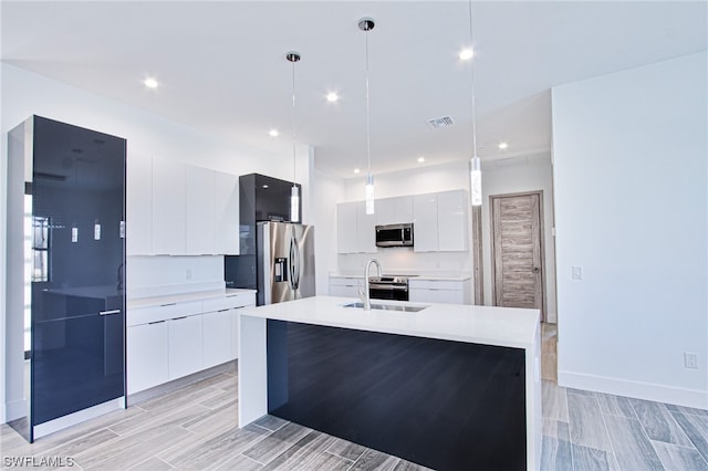 kitchen with hanging light fixtures, a kitchen island with sink, white cabinets, and appliances with stainless steel finishes