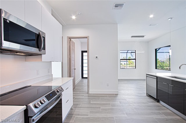 kitchen with a chandelier, stainless steel appliances, white cabinetry, and sink