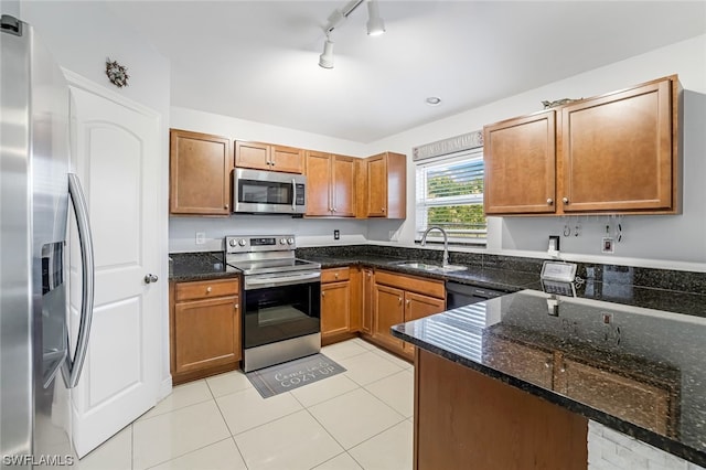 kitchen with dark stone counters, sink, appliances with stainless steel finishes, light tile patterned floors, and track lighting