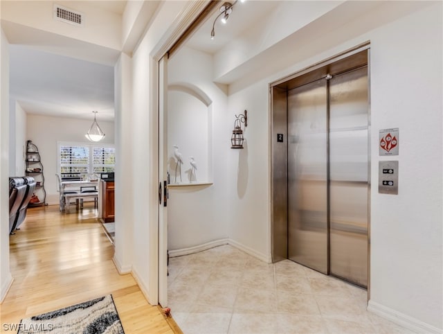 hall with elevator, light wood-type flooring, and track lighting