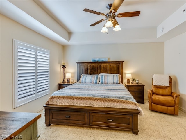 carpeted bedroom with a raised ceiling and ceiling fan