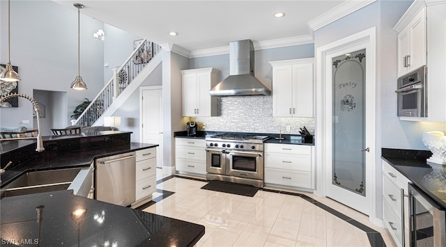 kitchen with appliances with stainless steel finishes, decorative light fixtures, wall chimney exhaust hood, and white cabinetry