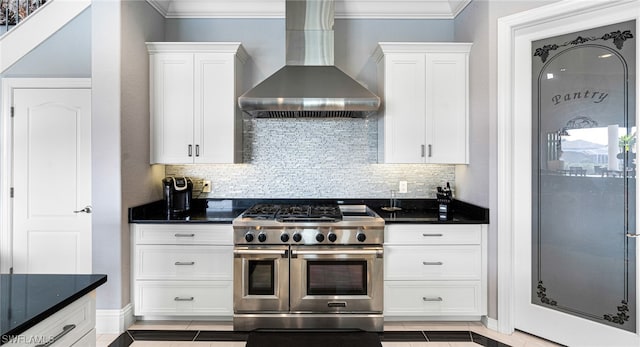 kitchen with wall chimney range hood, double oven range, white cabinets, and dark stone countertops