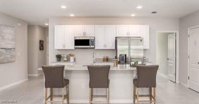 kitchen featuring appliances with stainless steel finishes, an island with sink, a breakfast bar area, white cabinets, and light stone counters