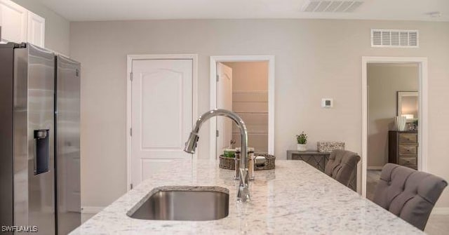 kitchen featuring stainless steel refrigerator with ice dispenser, a breakfast bar, sink, light stone counters, and white cabinets