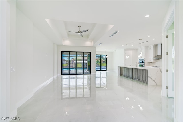 interior space featuring ceiling fan, sink, a raised ceiling, and light tile patterned floors