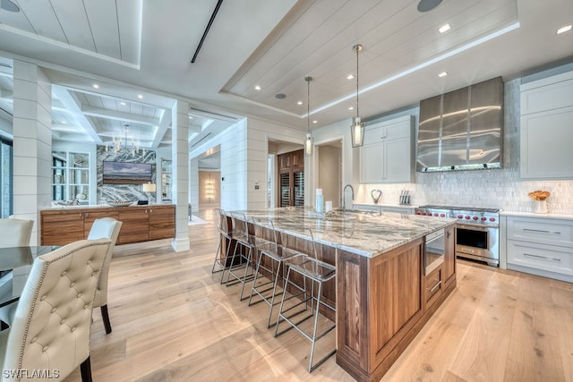 kitchen with light hardwood / wood-style floors, white cabinets, light stone counters, and a center island with sink