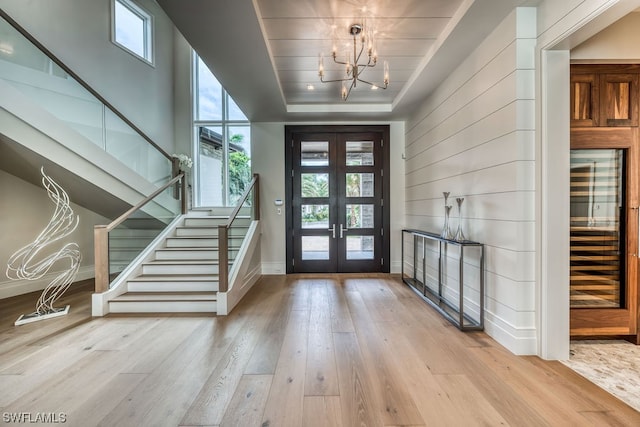 foyer entrance featuring french doors, light hardwood / wood-style floors, a healthy amount of sunlight, and a chandelier