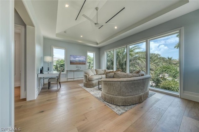 living room featuring plenty of natural light, ceiling fan, a tray ceiling, and light hardwood / wood-style flooring