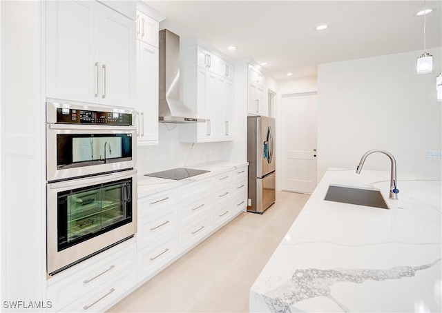 kitchen featuring appliances with stainless steel finishes, white cabinetry, sink, light stone counters, and wall chimney exhaust hood