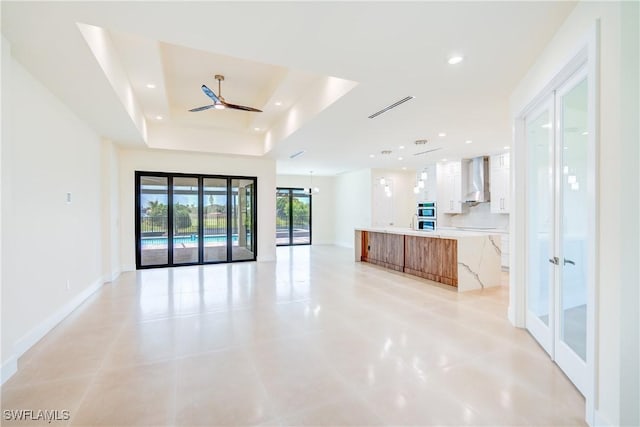 unfurnished living room with ceiling fan and a tray ceiling