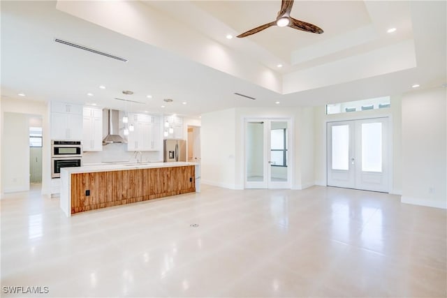 unfurnished living room with a raised ceiling, sink, ceiling fan, and french doors