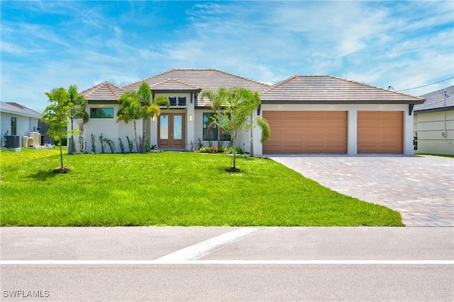 view of front of home with a garage, a front yard, central AC unit, and french doors