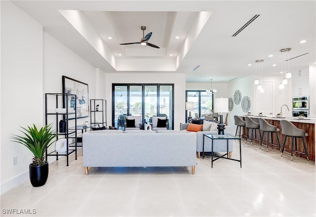 living area with recessed lighting, visible vents, a tray ceiling, ceiling fan with notable chandelier, and light tile patterned flooring