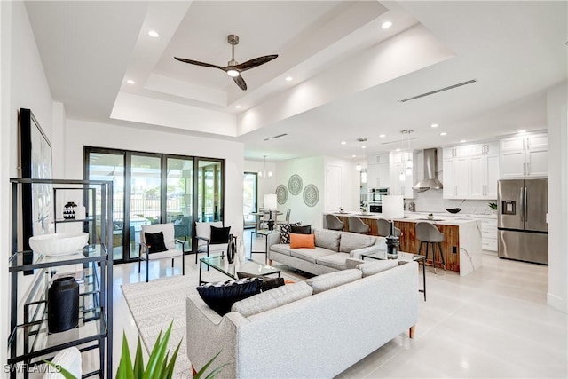 living area with a tray ceiling, a ceiling fan, visible vents, and recessed lighting